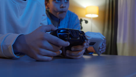 Close-Up-On-Hands-Of-Two-Young-Boys-At-Home-Playing-With-Computer-Games-Console-On-TV-Holding-Controllers-Late-At-Night-1